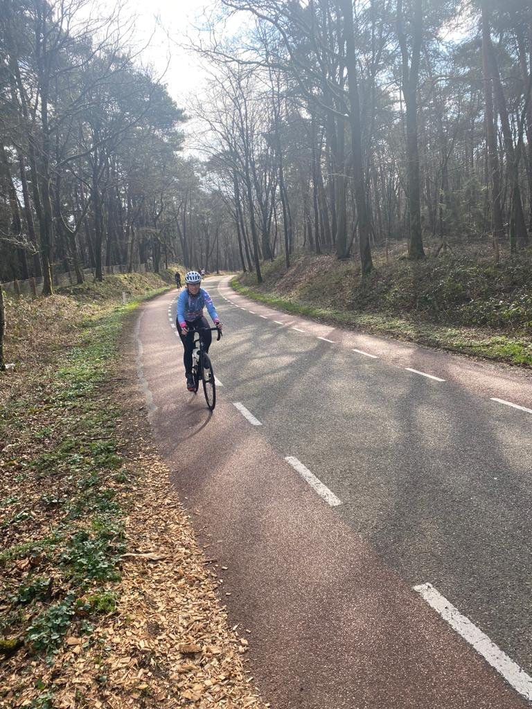 Vrouwelijke wielrenner op asfaltweg door een bos met kale bomen in het Nederlandse voorjaar