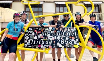Fietsers voor bord van Col du Lautaret in de Franse Alpen omlijst met een gele fiets
