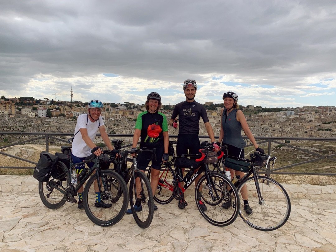 Groepsfoto met fietsers voor de stad Matera met de Sassi di Matera op de achtergrond