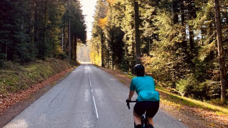 Fietser op asfaltweg in een bos met oranje en groene bladeren met zonnestralen door de bomen heen in de herfst