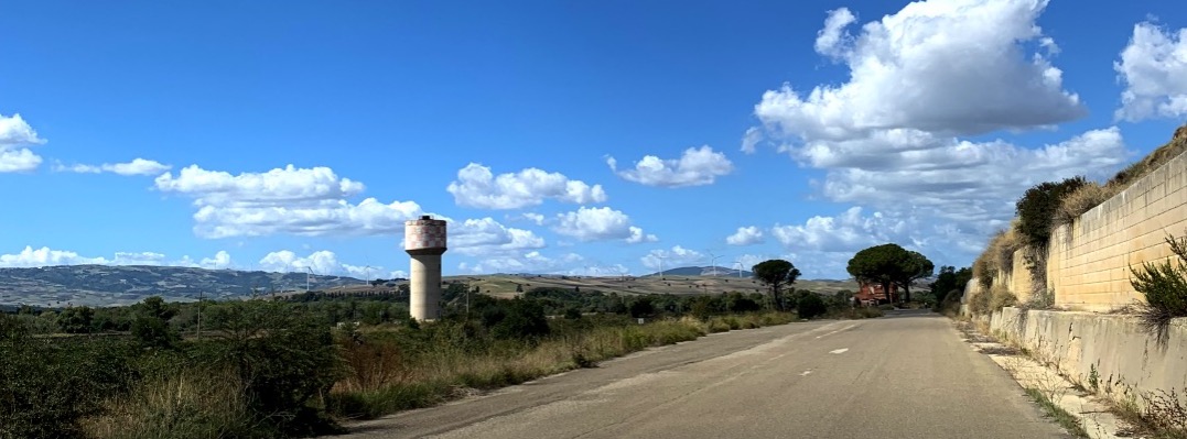 Weg in het landschap met watertoren wolken en typische bomen in binnenland Zuid Italië