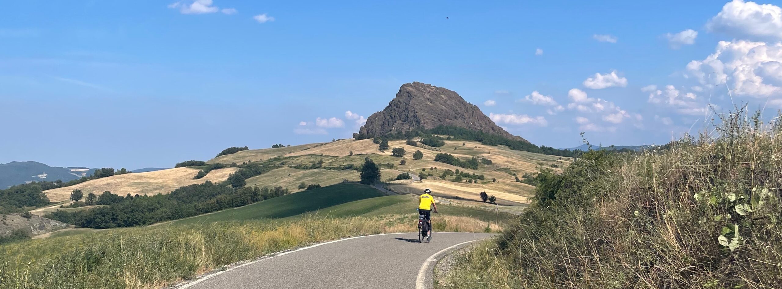 Fietser in glooiend landschap in Emilia Romagna Italië met op achtergrond rots Pietra Parcellara