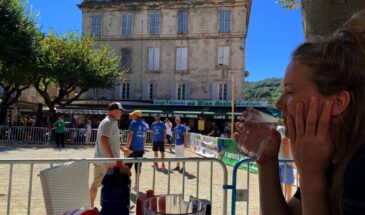 Vrouw drinkt een glas water met op de achtergrond Fransen die Jeu de Boules spelen