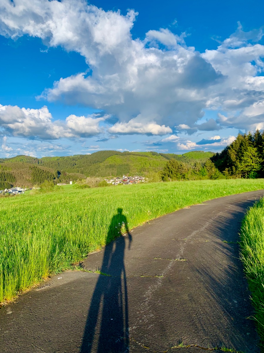 Fietsen op een fietspad in de vooravond in de Eifel met blauwe lucht, wolken en heel groen gras. Vlakbij Uedersdorf