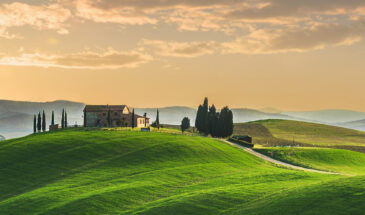 Glooiend heuvellandschap in Toscane bij zonsondergang met boerderij en cipressen.