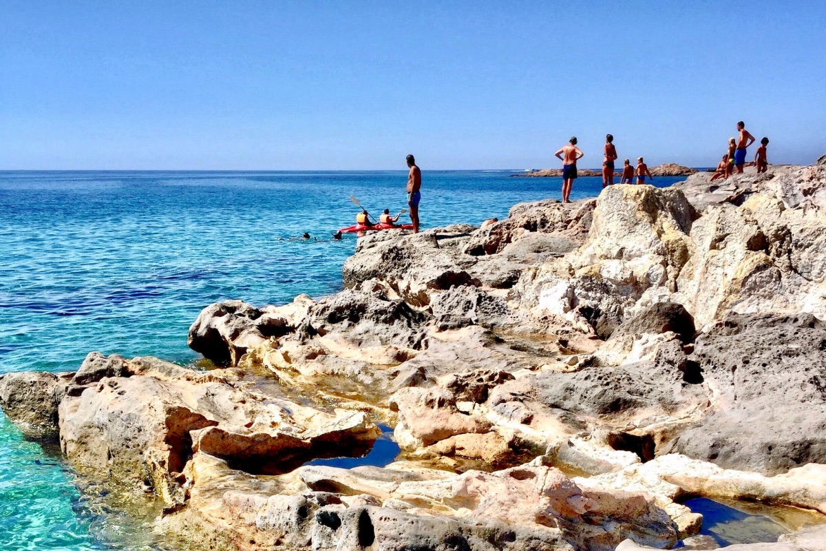Strand met rotsen op San Pietro eiland vlakbij Sardinië in de zon met zonnende mensen