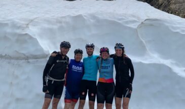 Groep wielrenners op Col du Galibier met op achtergrond veel sneeuw. In juni.