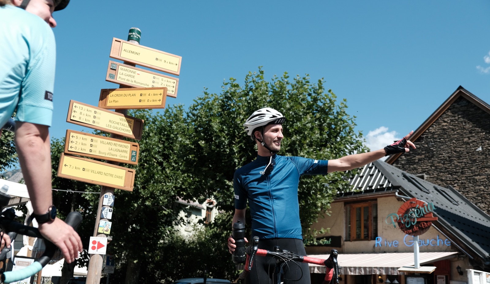 Wielrenner voor een wegwijzerbord in Bourg d'Oisans geeft uitleg