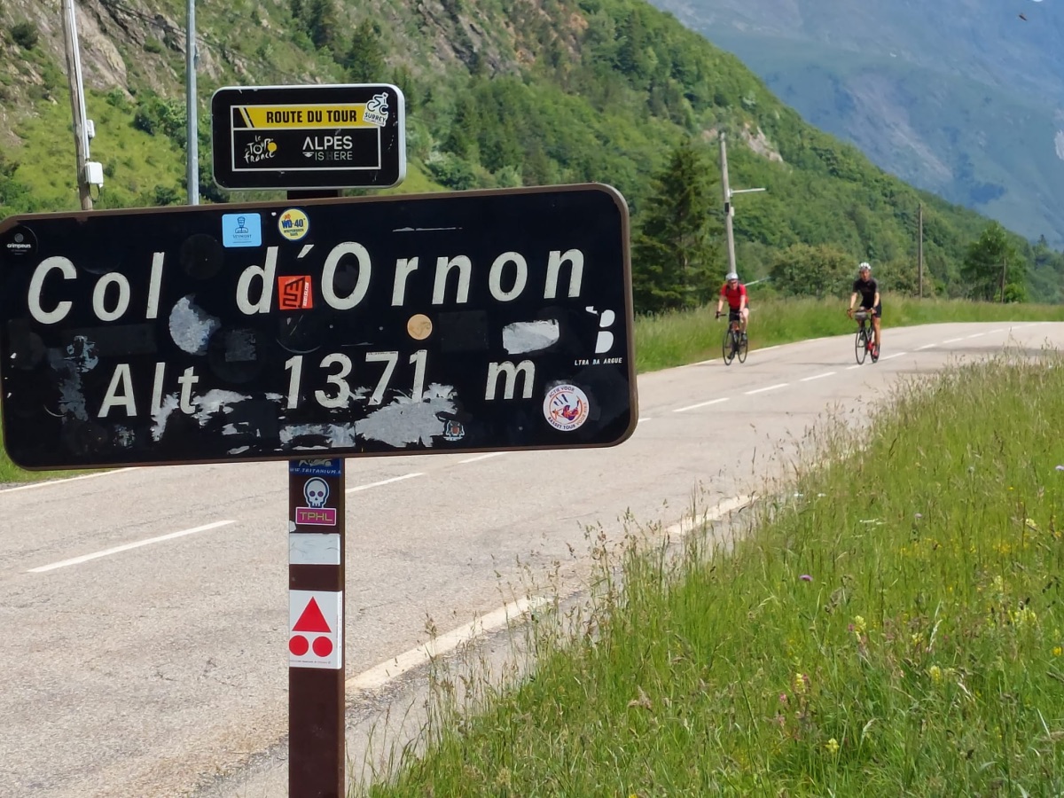Col d'Ornon colbord met op achtergrond twee wielrenners.