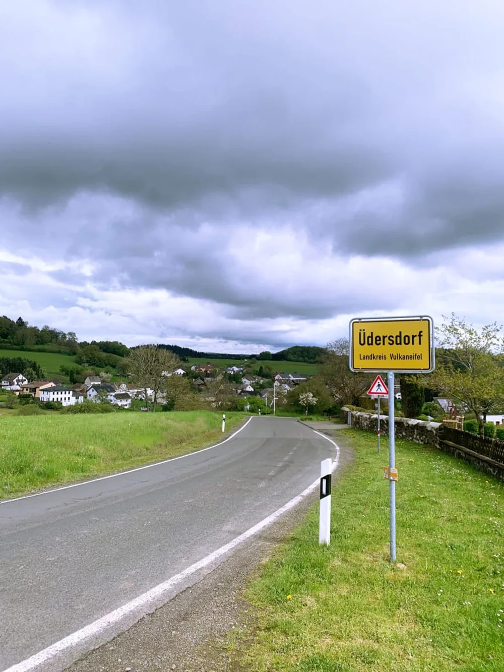 Eifel-Fietsen-voor-dagen-verticaal Fietsen op een fietspad in de vooravond in de Eifel met blauwe lucht, wolken en heel groen gras. Vlakbij Uedersdorf