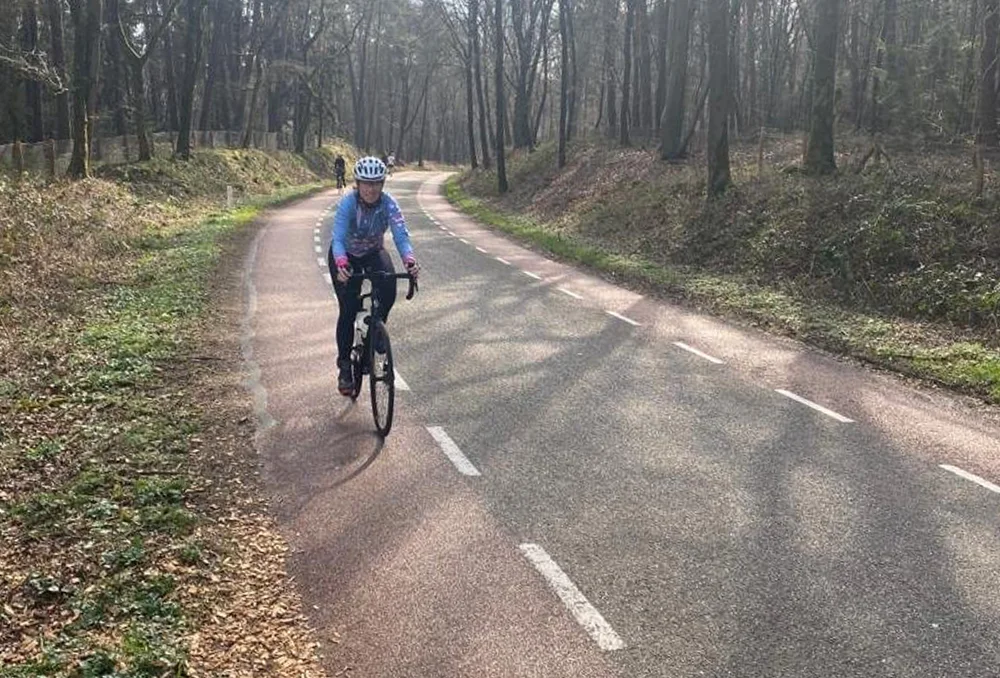 Nederland_Posbank_dames wielrenner in bos bij Beek aan de Peeskesweg in maart Vrouwelijke wielrenner op asfaltweg door een bos met kale bomen in het Nederlandse voorjaar