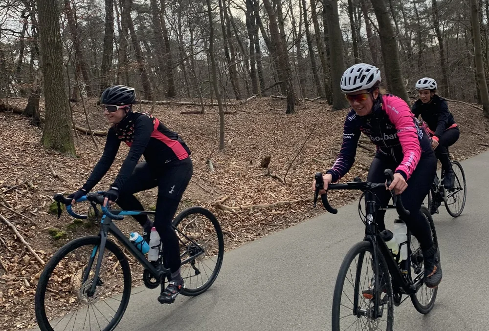 Nederland_Posbank_dames tijdens het wielrennen op de posbank in maart Fietsers in bos over asfaltweg in Gelderland in het voorjaar
